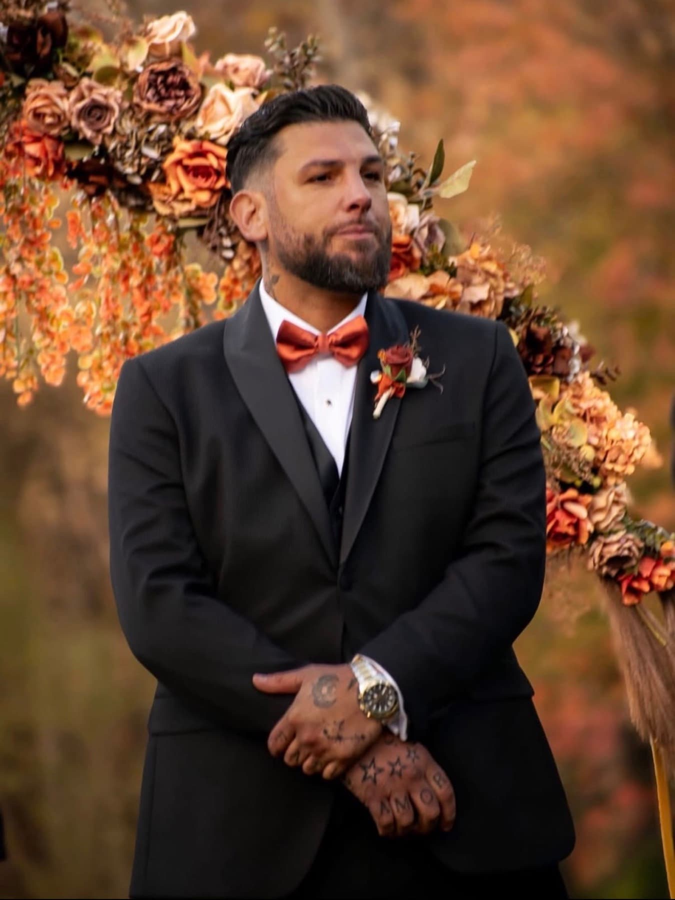 Groom in a black tuxedo under an autumn floral arch