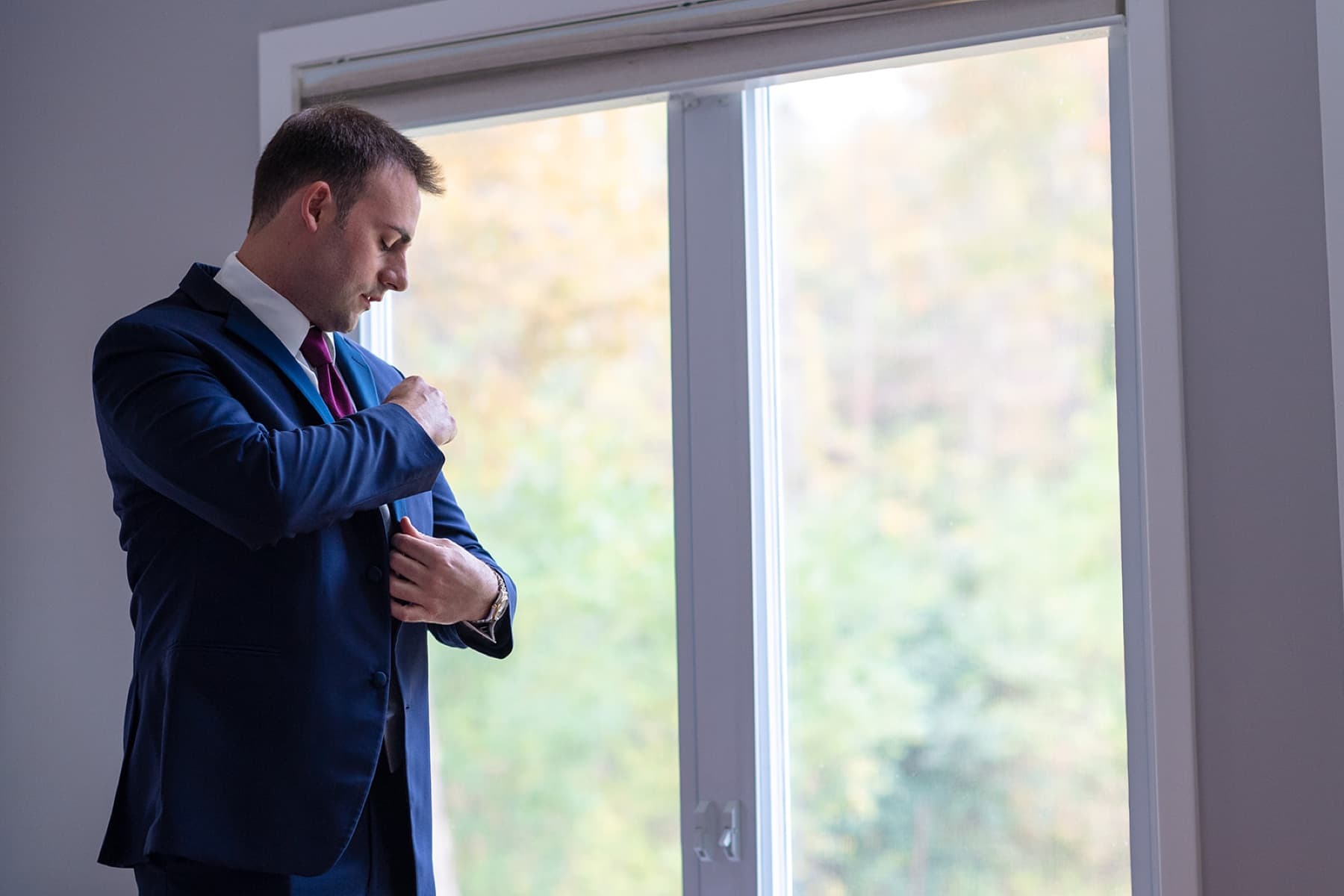 Groom adjusting his cuff by a window