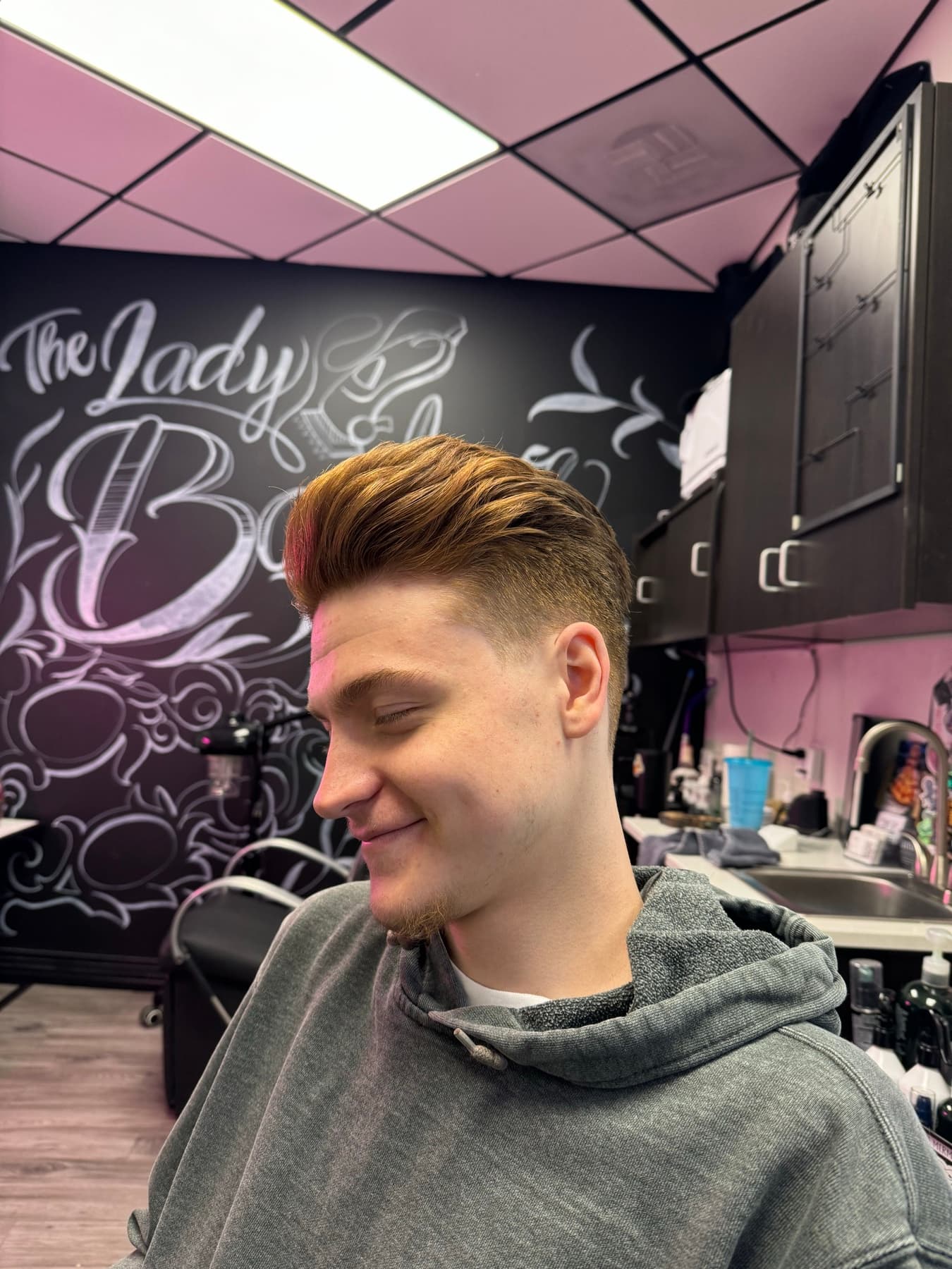 Client with a fresh pompadour in front of The Lady Barber mural wall